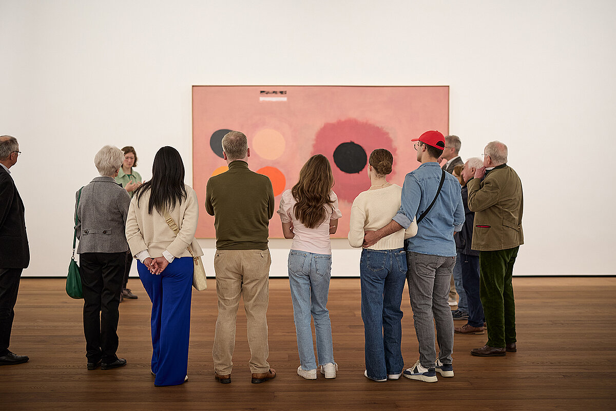 Foto einer Gruppe Menschen, die vor einem rosafarbenen abstrakten Kunstwerk stehen. Das Bild ist aufgenommen im Museum Rheinhard Ernst.